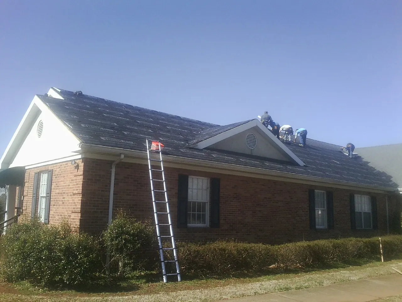 Crew tearing shingles off a brick ranch roof with a ladder set — Emergency Roof Repair work by our crew in Gerrardstown