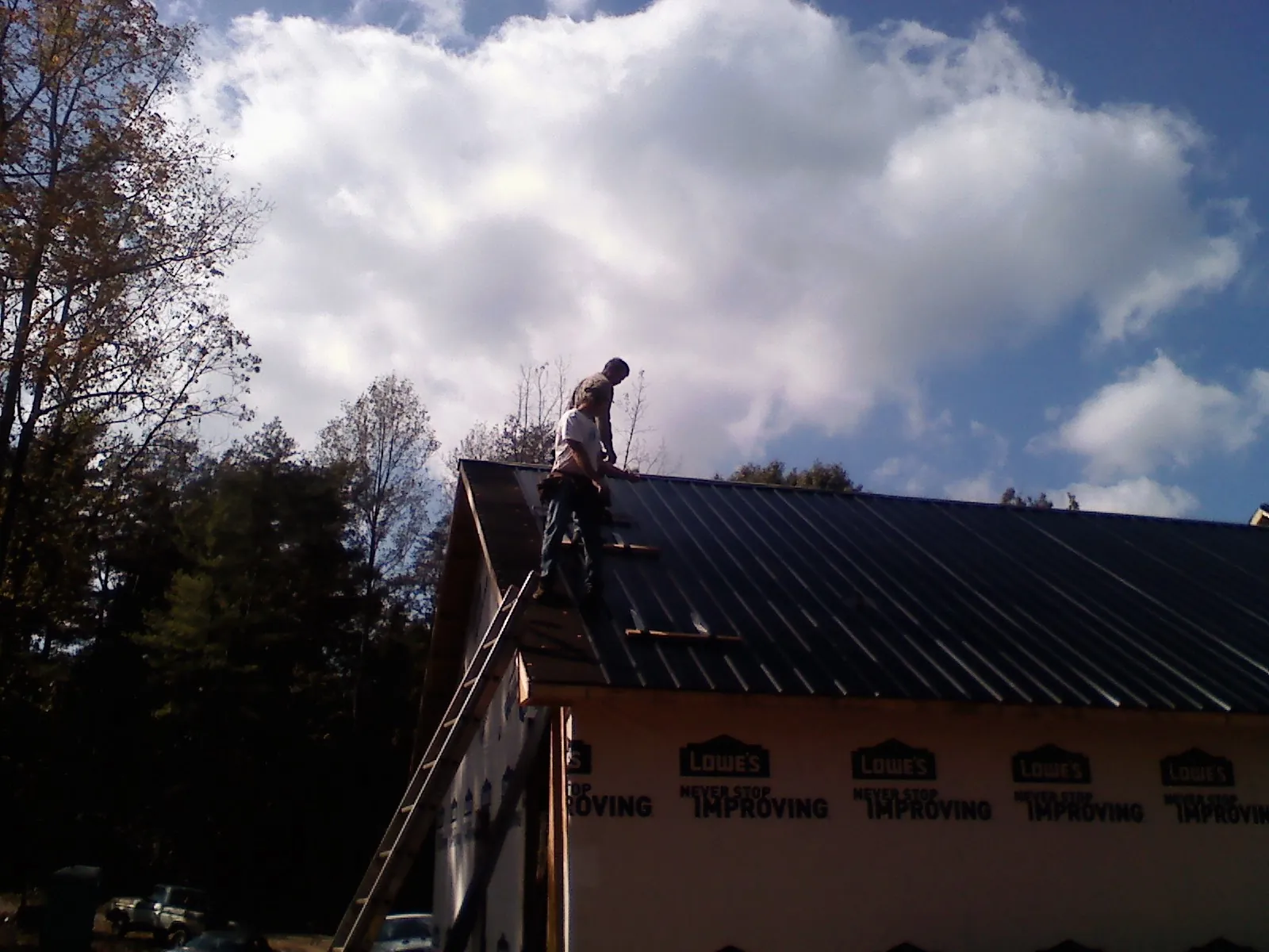 Roofer fastening dark metal panels high against a cloudy sky, from a Roof Inspection job in Gerrardstown