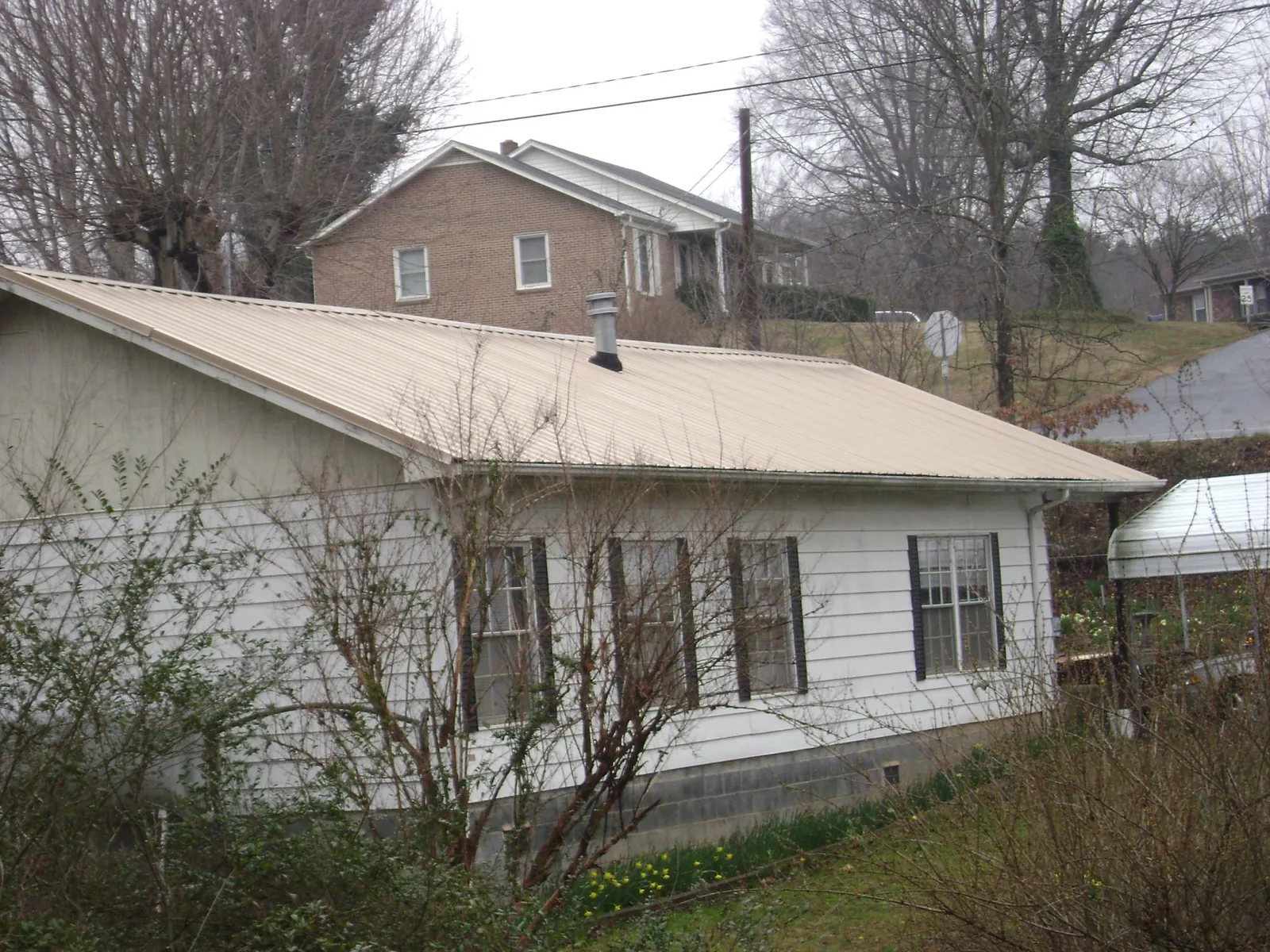 Tan metal roof on a white sided house set into a hillside — Commercial Roofing by Roofing Brothers in Gerrardstown